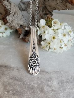 a silver necklace sitting on top of a table next to white flowers and a tree branch