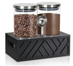 two glass jars filled with coffee beans on top of a black container and grinder