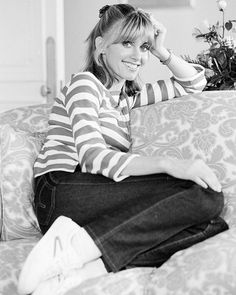 a black and white photo of a woman sitting on a couch with her hands behind her head