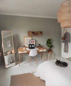 a cat laying on top of a white bed next to a mirror and desk in a bedroom