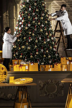 two people are decorating a christmas tree in a room with yellow boxes on the floor