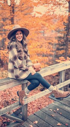 a woman sitting on top of a wooden bench wearing a hat and holding a purse