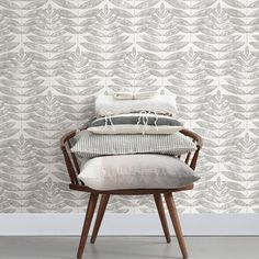 a chair with pillows on it in front of a wallpapered background that has leaves