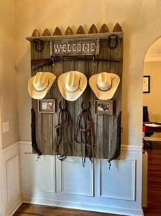 three cowboy hats hanging on a wall with the word welcome written above them and four other items in front of it