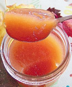 a spoon full of jelly sitting on top of a jar filled with liquid next to leaves