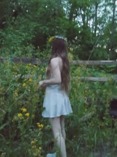 a woman standing in the grass with her back to the camera and looking at flowers