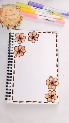 an open notebook with flowers on it next to markers and pencils