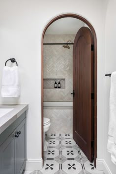 an arched doorway leads to a bathroom with white walls and flooring, along with black and white patterned tile