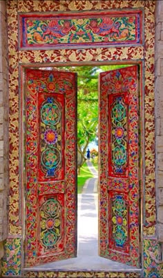 an intricately decorated door in the middle of a brick wall with trees and grass