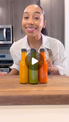 a woman sitting at a counter with three bottles of juice in front of her smiling