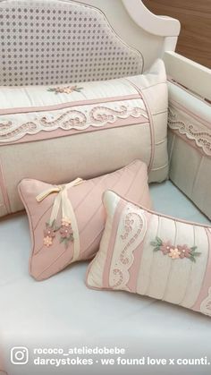 three decorative pillows on a white bed with pink trimmings and bows are sitting next to each other