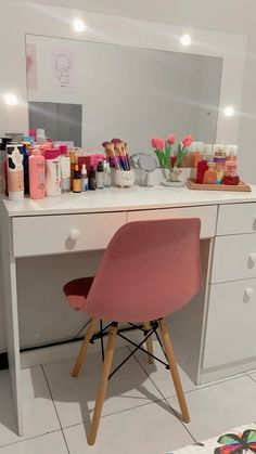 a pink chair sitting in front of a white desk with makeup and cosmetics on it