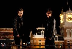 two young men standing next to each other in front of a clock tower at night