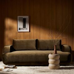 a living room with a couch, coffee table and vase on the floor in front of a wooden wall