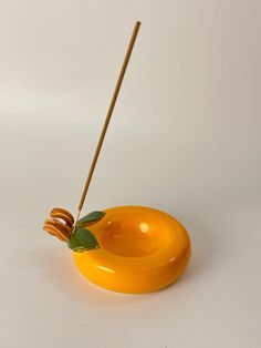 an orange object with a wooden stick sticking out of it's center and leaves on top