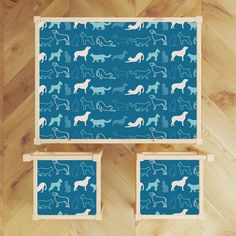 three pieces of blue and white art work with dogs on them, sitting on wood flooring