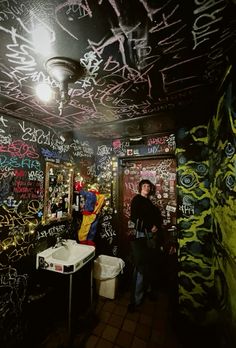 a person standing in a bathroom with graffiti all over the walls and ceiling, next to a sink