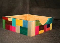 a wooden box made out of multicolored wood on a black background with the lid open