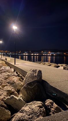 a street light on the side of a road next to rocks and water at night