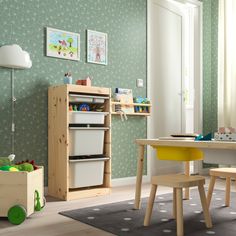 a child's room with green wallpaper and wooden furniture, including a toy storage unit