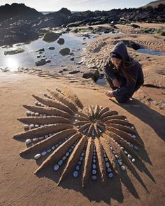 a woman kneeling down on top of a sandy beach next to an intricate sand sculpture