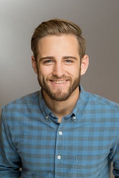 a man with a goatee smiles at the camera while wearing a blue plaid shirt