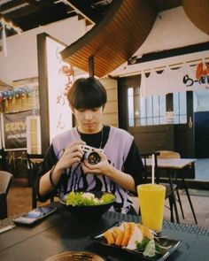 a person sitting at a table with food and a camera in front of them,