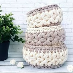 three crocheted baskets are stacked on top of each other next to a potted plant