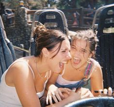 two girls are laughing while riding on a roller coaster