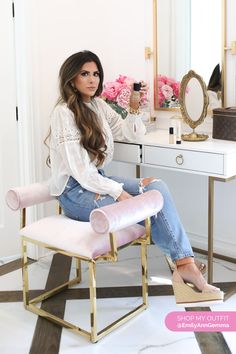 a woman sitting on a chair in front of a desk with a mirror and pink flowers