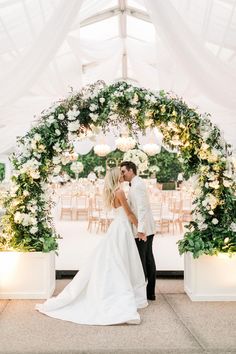 a bride and groom kissing under an archway decorated with white flowers at their wedding reception