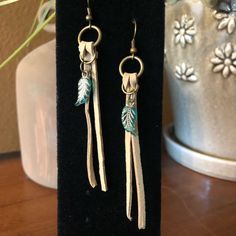 two pairs of earrings with leaves on them sitting on a black velvet stand next to a potted plant