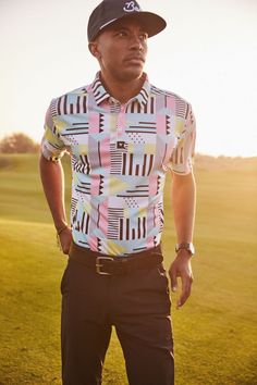 a man standing on top of a green field wearing a hat and shirt with geometric designs