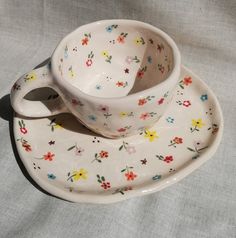 two cups and saucers are sitting on a white plate with flowered designs in them