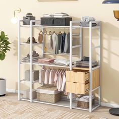 a white shelving unit with baskets and clothes on it's shelves next to a potted plant