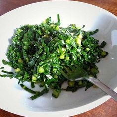 a white plate topped with green vegetables on top of a wooden table next to a fork