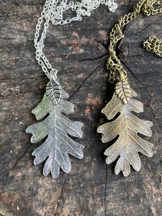 two silver and gold leaf necklaces sitting on top of a piece of tree trunk