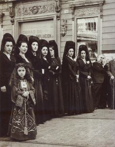 an old black and white photo of women standing in front of a building with long hair