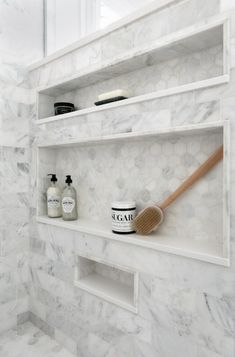 a bathroom with white marble walls and shelving holding various personal care items, including a wooden brush