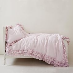 a white bed with pink ruffled sheets and pillows on it's side, against a wall