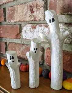 three white ceramic ghost figurines sitting on top of a wooden table next to a brick wall