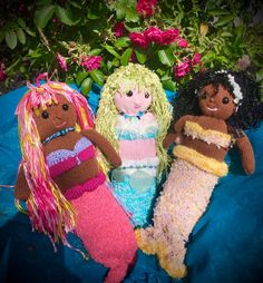 three knitted dolls sitting next to each other on a blue blanket with pink flowers in the background