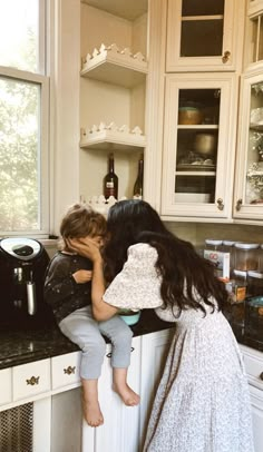 two young children are sitting on the counter in a kitchen, one is hugging the other's head