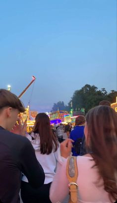 people standing around at an amusement park with rides in the back ground and fair goers looking on