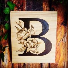 the letter b is decorated with flowers and leaves on a wooden surface, along with greenery