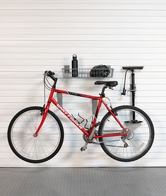 a red bicycle parked in front of a white garage door with tools on the rack