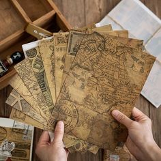 a person holding several pieces of old paper on top of a wooden table next to other items