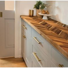 a wooden counter top in a kitchen next to a white door and cupboards with gold handles