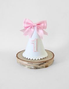 a white party hat with pink ribbon and number 1 on the top sitting on a piece of wood