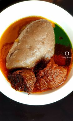 a white bowl filled with meat and gravy on top of a black table